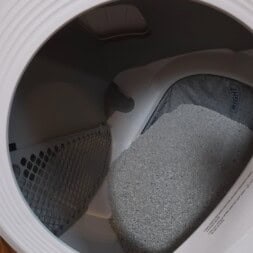 Automatic litter box test: Self-cleaning litter box without odor - Mova LR10 33 A close-up view of the inside of a litter box shows gray clumping litter piled at the bottom. The circular opening and plastic interior of the litter box are clearly visible. www.commaik.de