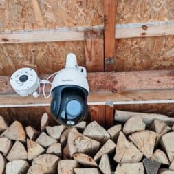The best Reolink 4k PTZ surveillance cameras in comparison: 823S2 vs 823S1 vs TrackMix vs TrackFlex in test 31 A Reolink 4K PTZ security camera is mounted on a wooden wall above a pile of cut firewood, flanked by two white round devices on either side. www.commaik.de