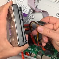 Expand Reolink NVR storage space - Installing and configuring hard disks correctly 21 A person's hands connect a SATA power and data cable to a hard disk in a Reolink NVR, with the inside of the device visible in the background. www.commaik.de