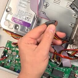 Expand Reolink NVR storage space - Installing and configuring hard disks correctly 27 A person's hands connect a power and data cable to a hard disk in an open Reolink NVR device with visible circuit boards and additional hard disks. www.commaik.de