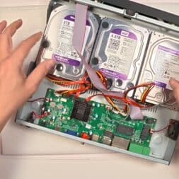 Expand Reolink NVR storage space - Installing and configuring hard disks correctly 29 Two hands install or connect cables to three hard drives in an opened Reolink NVR, exposing a green circuit board and various wires. www.commaik.de