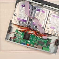 Expand Reolink NVR storage space - Installing and configuring hard disks correctly 30 An opened Reolink NVR housing reveals two 3TB hard disks connected via cables to a visible green circuit board with various components and connectors. The device rests on white foam padding. www.commaik.de