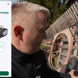 Lymow One Plus in test: RTK robot mower for large areas & difficult terrain 21 A person holds a smartphone outdoors near a wooden fence and pallets. The app screen displays instructions for pairing a Lymow One robotic lawnmower, which apply to both the Lymow One and the advanced Lymow One Plus model. www.commaik.de