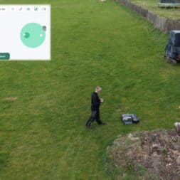Lymow One Plus in test: RTK robot mower for large areas & difficult terrain 28 A person stands on a lawn next to the Lymow One Plus robotic lawnmower and a pile of garbage with a device in his hand. An overlay shows the digital interface for adding a mowing zone. www.commaik.de