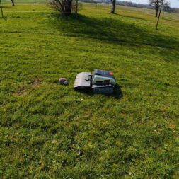 Lymow One Plus in test: RTK robot mower for large areas & difficult terrain 33 A Lymow One Plus robotic lawnmower and its charging station stand in a large, grassy field under a partly cloudy sky, with trees and a fence in the background. www.commaik.de