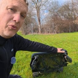 Lymow One Plus in test: RTK robot mower for large areas & difficult terrain 40 A person kneels in the grass and holds up a Lymow One Plus robotic lawnmower to show its underside. Trees, a fence and houses can be seen in the background on a sunny day. www.commaik.de