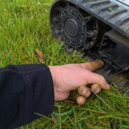 Lymow One Plus in test: RTK robot mower for large areas & difficult terrain 50 A person wearing a dark sleeve points to a part inside the track of a Lymow One Plus robotic lawnmower standing on green grass. www.commaik.de