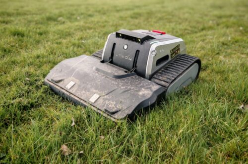 Lymow One Plus in test: RTK robot mower for large areas & difficult terrain 3 A Lymow One Plus robotic lawnmower with tank-like tracks sits on green grass, slightly dirty from use, in an outdoor area. www.commaik.de