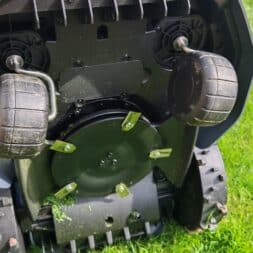Robot lawn mower without boundary wire in test: LiDAR vs RTK in comparison (ANTHBOT M5 vs M9) 7 Close-up of the underside of an Anthbot robotic lawnmower on green grass. The wheels, the rotating blade unit and the grass clippings that get caught in various places should be emphasized. www.commaik.de