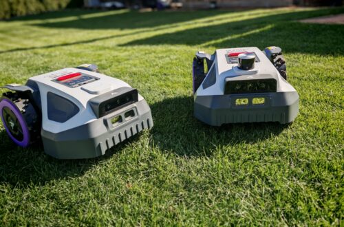 Robot lawn mower without boundary wire in test: LiDAR vs RTK in comparison (ANTHBOT M5 vs M9) 3 Two Anthbot robotic lawnmowers stand side by side on green grass, the sunlight illuminating their wheels and sensors in a backyard or garden. www.commaik.de