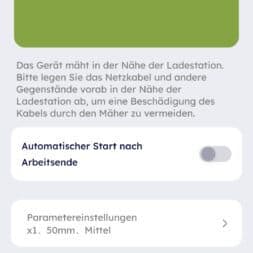 Robot lawn mower without boundary wire in test: LiDAR vs RTK in comparison (ANTHBOT M5 vs M9) 33 A smartphone screen shows instructions in German for operating the Anthbot robotic lawnmower near the charging station, with a picture of the mower and the station as well as options for automatic start and parameter settings. www.commaik.de