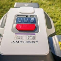 Robot lawn mower without boundary wire in test: LiDAR vs RTK in comparison (ANTHBOT M5 vs M9) 9 Close-up of an Anthbot robotic lawnmower in a meadow, showing a prominent red stop button, control panel, warnings and instructional images. www.commaik.de