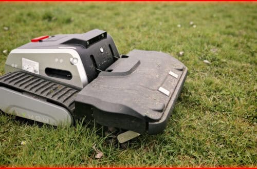 Lymow One Plus in test: robotic mower for large areas with 45° incline, RTK & chain drive A robotic mower with tank-like treads sits on a large, green area. The black and silver robot lawn mower, ideal for large areas thanks to RTK technology, shows grass clippings on the outer shell. A red frame surrounds the picture. www.commaik.de