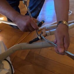 Installing Air Conditioning Yourself in an Older Building – Heating and Cooling in Practice 26 A person is using two wrenches to connect pipes on an air conditioning unit on a wooden floor. The person's hands and arms are visible, with the focus on the installation process. www.commaik.de