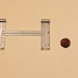 Installing Air Conditioning Yourself in an Older Building – Heating and Cooling in Practice 37 A metal TV mount is attached to a beige wall. To the right of the bracket, there is a round hole in the wall—possibly for an air conditioner—through which a dark room can be seen behind it. www.commaik.de
