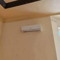Installing Air Conditioning Yourself in an Older Building – Heating and Cooling in Practice 60 Beneath a decorative ceiling with dark wood paneling and ornate swirl patterns, a beige, wall-mounted air conditioner is installed; two light bulbs are recessed into the ceiling. www.commaik.de