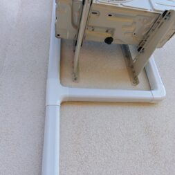 Installing Air Conditioning Yourself in an Older Building – Heating and Cooling in Practice 53 An air conditioner mounted high on an exterior wall, with white plastic pipes running vertically and horizontally beneath it to conceal cables or wires. www.commaik.de