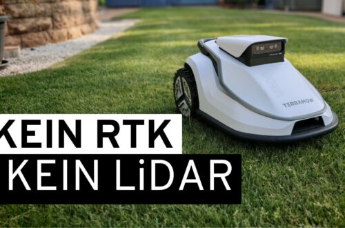 TerraMow V600 Review – A Robotic Lawn Mower Without RTK, LiDAR, or a Perimeter Wire Put to the Test A white robotic lawn mower—specifically, the TerraMow V600—is standing on a green lawn. A large text overlay reads: “NO RTK, NO LiDAR.” A stone wall and a building can be seen in the blurred background, which underscores the scene's realistic, real-world test setting. www.commaik.de