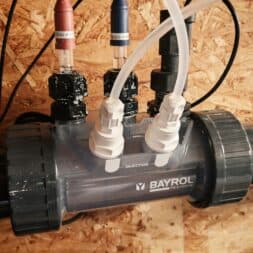 Installing the BAYROL Automatic Cl-pH in the Pool and Retrofitting a Temperature Sensor: My Experience 16 A close-up of a Bayrol Technic water injection system with connected hoses and cables, mounted on a wooden board, illustrating the precision engineering behind Bayrol's automated solutions. www.commaik.de