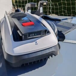 ECOVACS GOAT O1200 LiDAR PRO Review: Perfect Edge Mowing Without Any Touch-Ups? 8 A close-up of an outdoor robot like the Ecovacs Goat with brushes, standing on a glass table next to a sports net; green grass and a potted plant are visible in the background. www.commaik.de