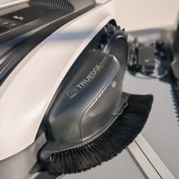 ECOVACS GOAT O1200 LiDAR PRO Review: Perfect Edge Mowing Without Any Touch-Ups? 12 Close-up of a robot vacuum cleaner with a visible side brush labeled “TrueEdge.” The device, which is reminiscent of the sleek design of Ecovacs Goat products, is primarily white and black and sits on a gray surface next to its accessories. www.commaik.de