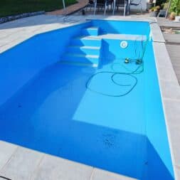 High Chlorine Consumption in the Pool: Why 20 Liters of Chlorine Disappeared in Two Weeks 52 A partially filled blue swimming pool with a set of stairs, a garden hose, and some dirt on the bottom. The pool is surrounded by tiles and a patio; next to it, chairs and plants bask in the sunlight. The scene suggests that cleaning or maintenance was recently performed, likely to regulate chlorine usage and ensure water quality for swimming. www.commaik.de