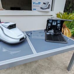 TerraMow V1000, V600, and Mini 500 Review: Robotic Lawn Mowers Without RTK and Lidar? 13 A white Terramow V1000 robotic lawn mower and its charging station are sitting on a gray garden table near a modern patio with plants; a house can be seen in the background. www.commaik.de