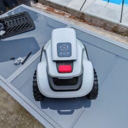 TerraMow V1000, V600, and Mini 500 Review: Robotic Lawn Mowers Without RTK and Lidar? 16 A Terramow V600 robotic lawn mower is sitting on a gray garden table next to a pool, with a few tools and a grill next to it. In the background, you can see green plants and a patio with lounge chairs. www.commaik.de