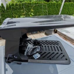 TerraMow V1000, V600, and Mini 500 Review: Robotic Lawn Mowers Without RTK and Lidar? 18 A large, sleek, gray, fin-shaped device resembling the innovative Terramow V1000 robotic lawn mower stands on a patio near a pool and lounge chairs, with green plants in the background and various cables and parts lying on its base. www.commaik.de