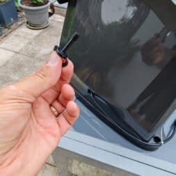 TerraMow V1000, V600, and Mini 500 Review: Robotic Lawn Mowers Without RTK and Lidar? 17 A hand is holding a black plastic cap near a dark, curved part of a robotic lawn mower—possibly a Terramow V1000 or Terramow V600 model—outdoors on a patio, with plants and the garden visible in the background. www.commaik.de