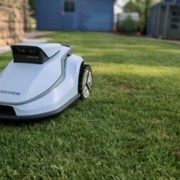 TerraMow V1000, V600, and Mini 500 Review: Robotic Lawn Mowers Without RTK and Lidar? 12 A Terramow V600 robotic lawn mower bearing the inscription “TERRAMOW” is mowing the grass in a well-manicured garden; in the background, a stone wall, a small building, and a blue shed are visible. www.commaik.de