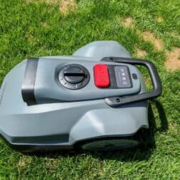 TerraMow V1000, V600, and Mini 500 Review: Robotic Lawn Mowers Without RTK and Lidar? 29 A gray robotic lawn mower, the Terramow V1000, with a red stop button, is standing on green grass next to a patch of dry, brown grass. www.commaik.de