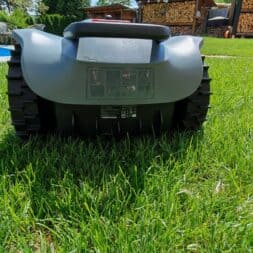 TerraMow V1000, V600, and Mini 500 Review: Robotic Lawn Mowers Without RTK and Lidar? 30 A Terramow V1000 robotic lawn mower is standing on a green lawn near a swimming pool and a stack of wood, seen from behind on a sunny day. www.commaik.de