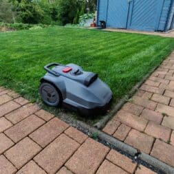 TerraMow V1000, V600, and Mini 500 Review: Robotic Lawn Mowers Without RTK and Lidar? 34 A Terramow V600 robotic mower is in operation on a well-maintained lawn bordered by brick paths, with a blue garden shed nearby and trees and shrubs visible in the background. www.commaik.de