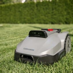 TerraMow V1000, V600, and Mini 500 Review: Robotic Lawn Mowers Without RTK and Lidar? 26 A silver robotic lawn mower called the “Terramow V1000” stands on a neatly mowed lawn; a green hedge and trees can be seen in the out-of-focus background. www.commaik.de