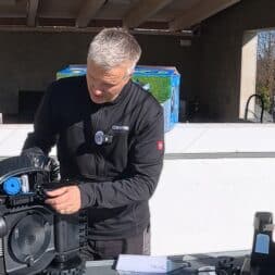 ECOVACS GOAT O1200 LiDAR PRO Review: Perfect Edge Mowing Without Any Touch-Ups? 14 A person with short, gray hair is examining and adjusting the interior of a large black mechanical device outdoors; they may be performing maintenance on an ECOVACS GOAT model, with tools and manuals lying on the table nearby. www.commaik.de