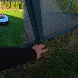 ECOVACS GOAT O1200 LiDAR PRO Review: Perfect Edge Mowing Without Any Touch-Ups? 48 A hand touches the base of a glass greenhouse on a lawn; an ECOVACS GOAT robotic lawn mower can be seen in the background. www.commaik.de