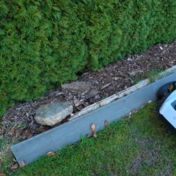 ECOVACS GOAT O1200 LiDAR PRO Review: Perfect Edge Mowing Without Any Touch-Ups? 51 An Ecovacs Goat robotic lawn mower is standing on the lawn next to a garden bed bordered by wooden planks and dense green shrubs. www.commaik.de