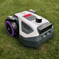 Mähroboter winterfest machen: Akku, Ladestation und RTK richtig überwintern 4 Ein weiß-grauer Winterfest-Mähroboter mit violetten Rädern auf einem grasbewachsenen Rasen. www.commaik.de