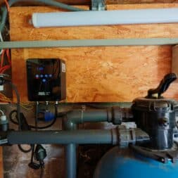 Frequenzumrichter Poolpumpe: Einbau, Einstellungen und Strom sparen 7 Ein AquaForte-Frequenzumrichter, montiert an einer Holzwand über einer Schwimmbadfilteranlage mit Rohrleitungen und einem blauen Behälter. www.commaik.de