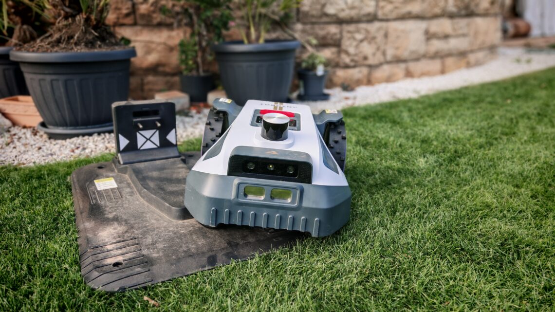 Mähroboter winterfest machen: Akku, Ladestation und RTK richtig überwintern 1 Ein Mähroboter, der auf seiner Ladestation in einem Rasenparkiert ist und bereit ist, für die Wintermonate vorbereitet zu werden, während Sie den Mähroboter überwintern. www.commaik.de