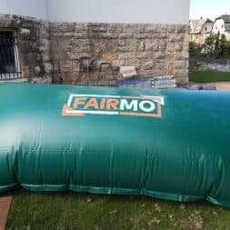 Pool winterfest machen: Wasser ablassen, Technik einlagern und das Becken abdecken 48 Große grüne aufblasbare FAIRMO-Wasserspeicherblase für die Überwinterung des Pools, die auf einer Rasenfläche vor einem Steingebäude steht. www.commaik.de