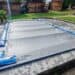 Pool winterfest machen: Wasser ablassen, Technik einlagern und das Becken abdecken 26 Ein rechteckiges Schwimmbecken, das für das Pool Winterfest vorbereitet wurde: Es ist mit einer grauen Plane abgedeckt, die mit blauen Wasserschläuchen auf einer Steinterrasse befestigt ist. www.commaik.de