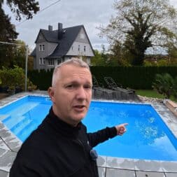 Pool winterfest machen: Wasser ablassen, Technik einlagern und das Becken abdecken 64 Ein Mann steht vor einem blauen Swimmingpool im Hinterhof und zeigt während des Pool-Winterfestes auf das Wasser. www.commaik.de